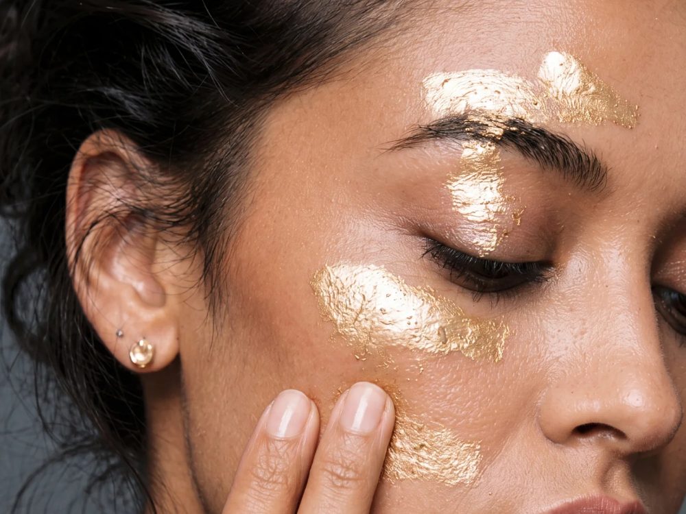 Close-up of a model with gold skincare swept across her cheek and brow